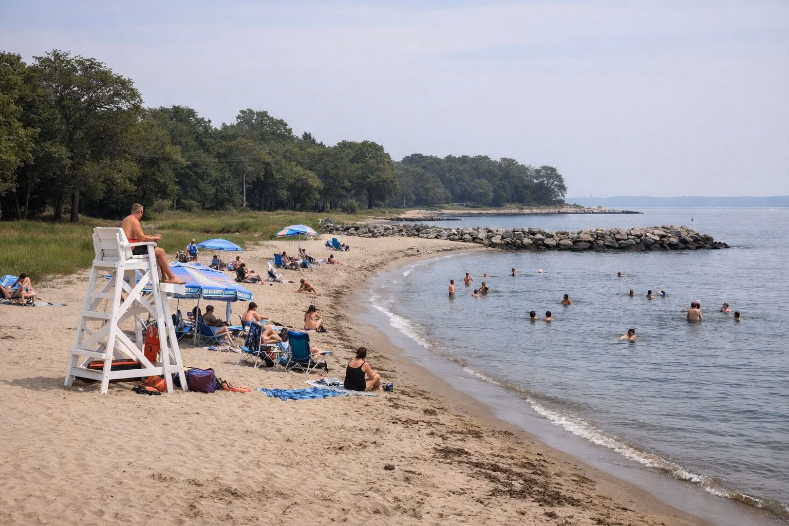 A busy town beach on Long Island Sound with a lifeguard stand, swimmers and umbrellas, a curving shoreline
