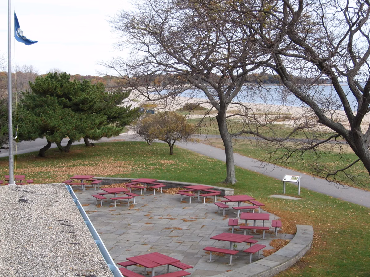 Picnic terrace with tables and a walkway seen from above, beach and water behind