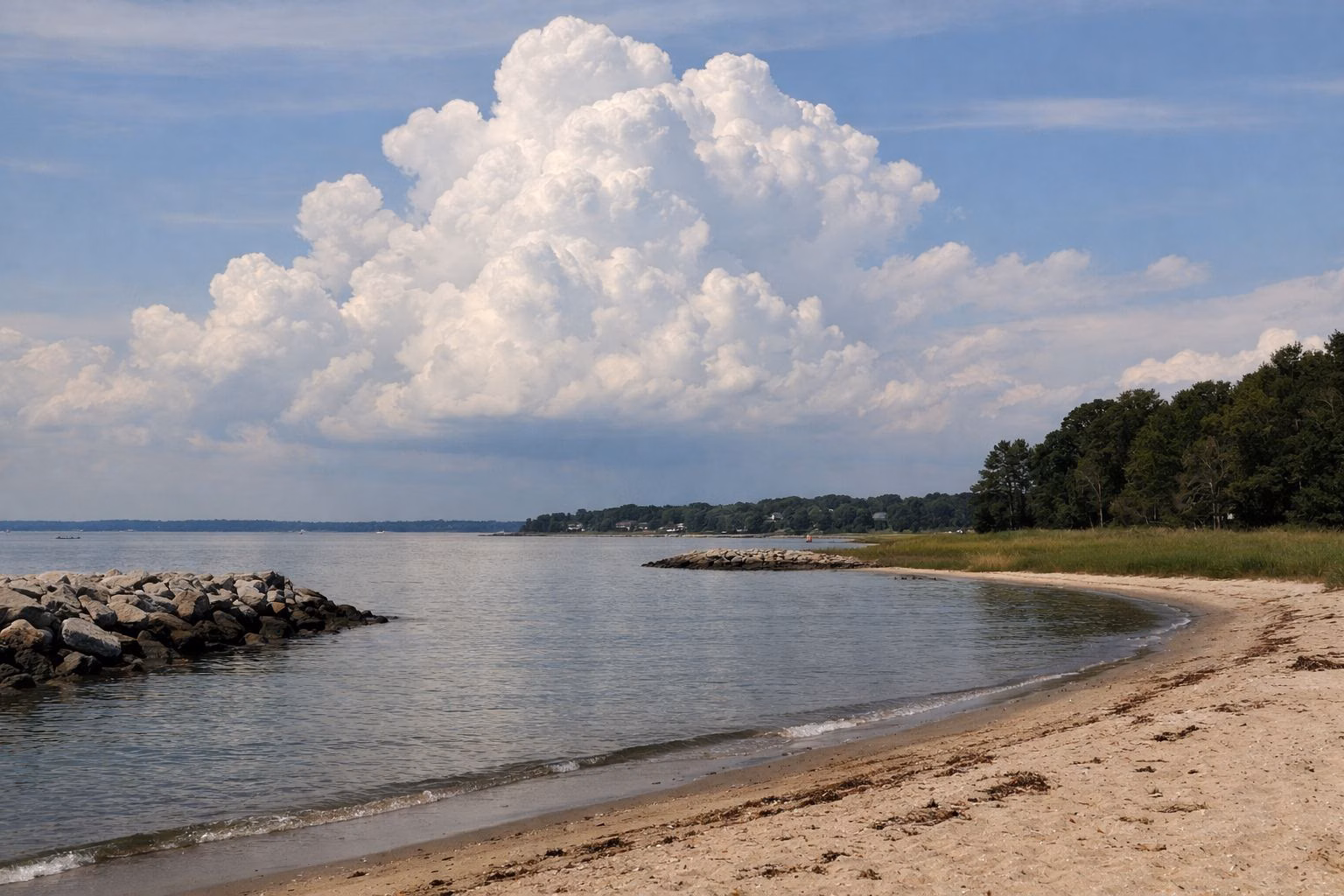 Tall summer cumulus clouds building over calm water seen from a sandy beach