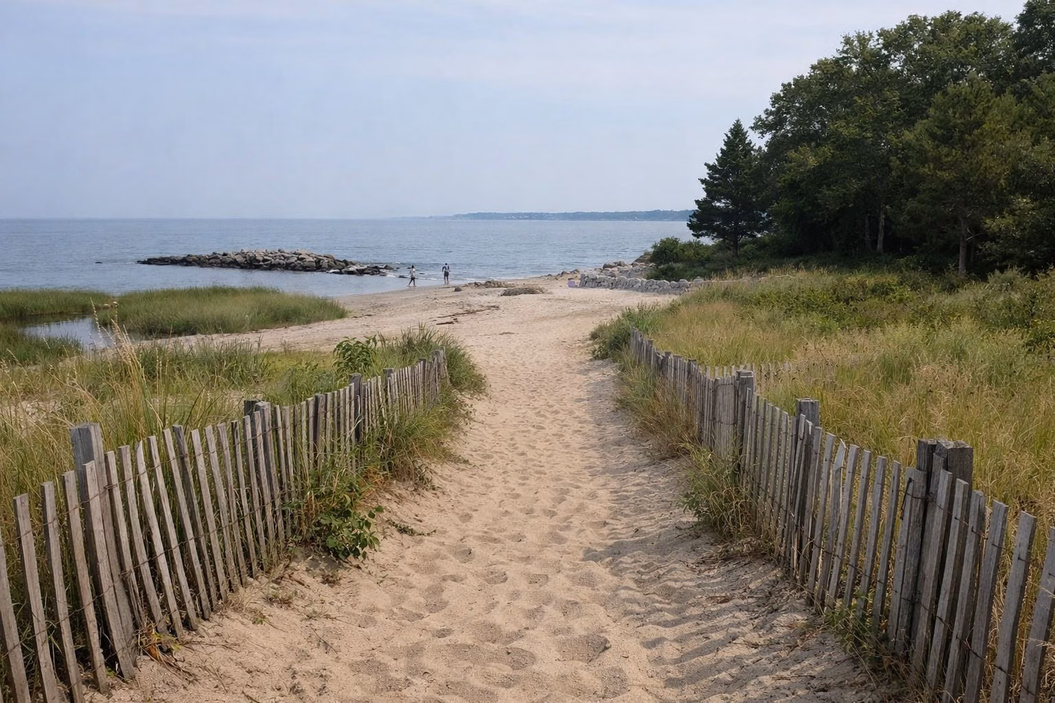 A sandy path between low wooden dune fencing leading to a beach