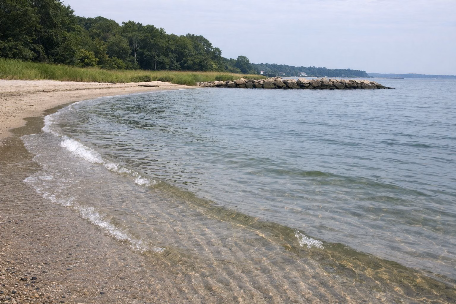 Clear shallow water over rippled sand at the water's edge, small waves, bright overcast
