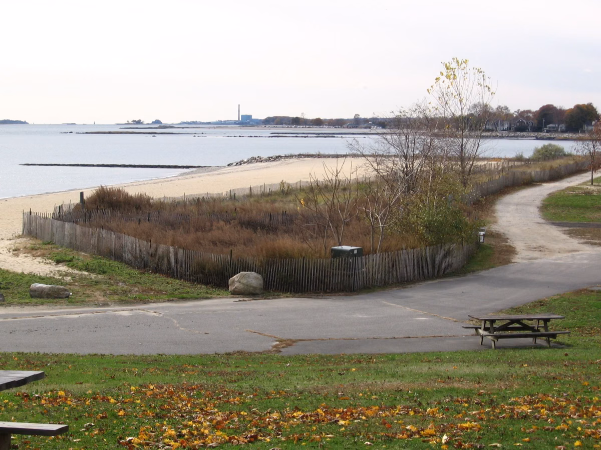 Paved path curving past a fenced dune area to the beach, Long Island Sound beyond